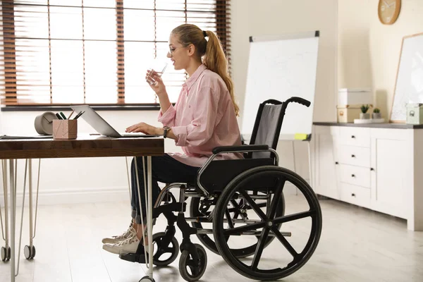 Vrouw in rolstoel drinkwater op de werkplek — Stockfoto