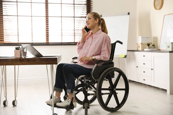 Vrouw in rolstoel praten op de telefoon aan tafel binnenshuis — Stockfoto