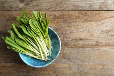 Ahşap masa üzerinde vahşi sarımsak veya RAMSON ile kase, üst görünüm. Metin alanı