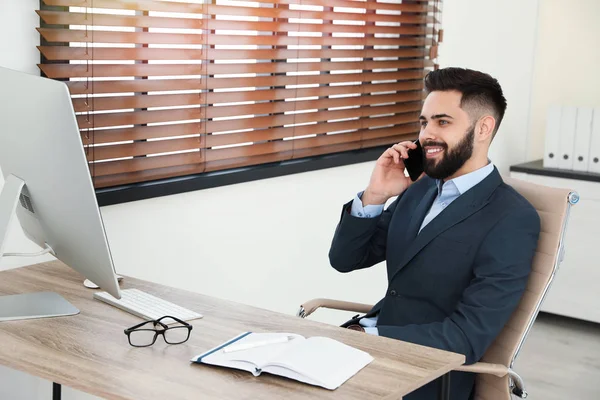 Красивий бізнесмен розмовляє по телефону під час роботи з комп'ютером за столом в офісі — стокове фото