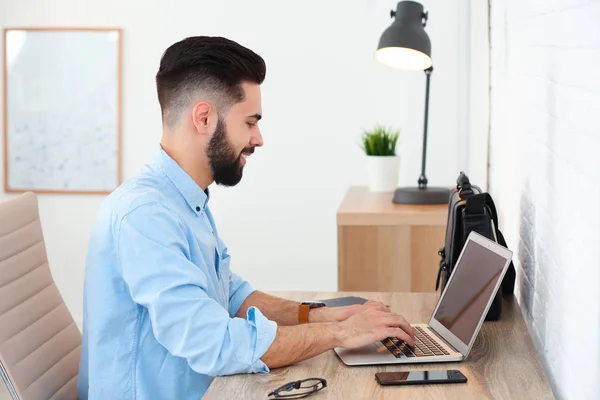 Guapo joven que trabaja con el ordenador portátil en la mesa en la oficina en casa —  Fotos de Stock