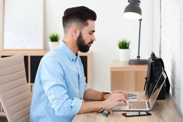 Beau jeune homme travaillant avec un ordinateur portable à la table dans le bureau à la maison — Photo