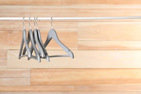 Metal rack with clothes hangers on wooden background, space for text — Stock Photo, Image