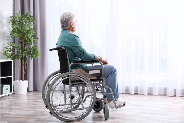 Homem idoso sentado em cadeira de rodas perto da janela em casa — Fotografia de Stock