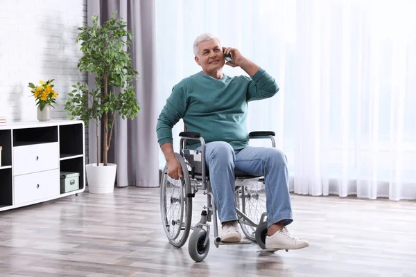 Старший в инвалидной коляске разговаривает по телефону дома — стоковое фото