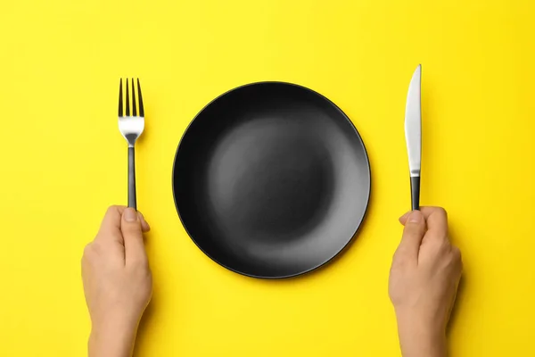 Donna con forchetta, coltello e piatto vuoto su sfondo a colori, vista dall'alto — Foto Stock