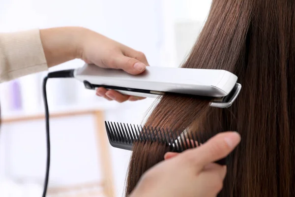 Coafeză folosind fier plat modern pentru a stila părul clientului în salon, closeup — Fotografie, imagine de stoc