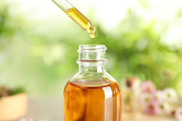 Goteo de aceite esencial de árbol de té natural en botella sobre fondo borroso, primer plano — Foto de Stock
