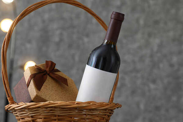Wicker basket with bottle of wine and gift box on table. Space for design