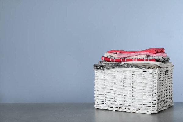 Wicker laundry basket with clean towels on table against color background. Space for text