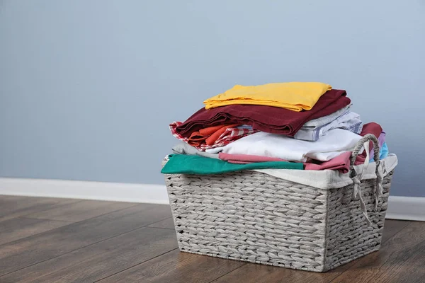 Wicker vasketøjskurv med rent tøj på gulvet nær farvevæg. Plads til tekst - Stock-foto