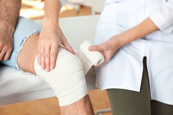 Врач накладывает повязку на колено пациента в клинике, крупным планом — стоковое фото