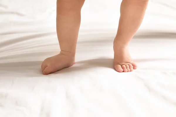 Cute little baby standing on white bed sheet, closeup — Stock Photo, Image