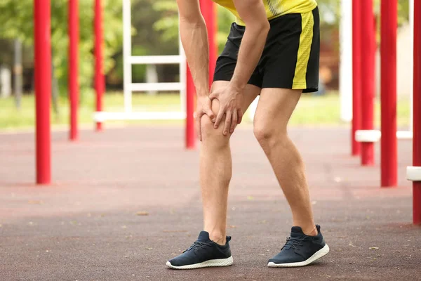 Young man suffering from knee pain on sports ground, closeup — Stock Photo, Image