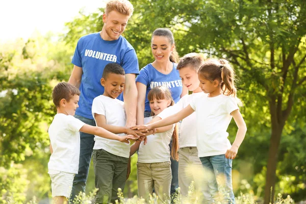 Grupp av barn att gå med händerna med volontärer i parken — Stockfoto
