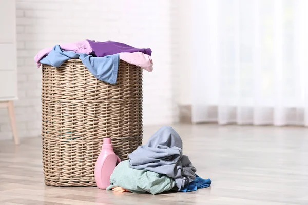 Rieten wasgoed mand met vuile kleren en wasmiddel op de vloer binnenshuis. Ruimte voor tekst — Stockfoto