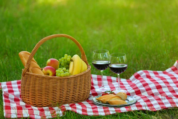 Cesta de vime com comida e vinho em cobertor no parque, espaço para texto. Piquenique de verão — Fotografia de Stock