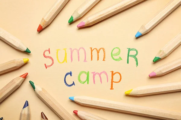 Text SUMMER CAMP and pencils on color background, flat lay