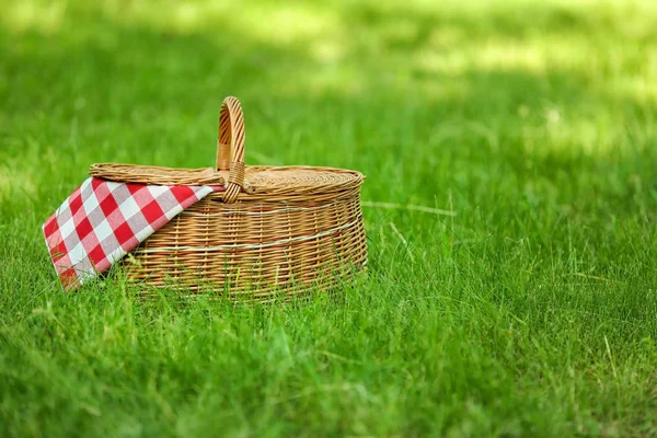 Panier en osier avec couverture sur herbe verte dans le parc, espace pour le texte. Pique-nique d'été — Photo