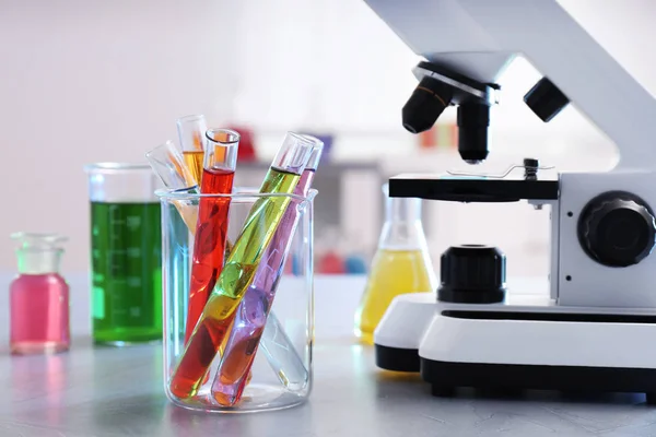 Becher con provette vicino al microscopio sul tavolo. Oggetti di vetro di chimica — Foto Stock