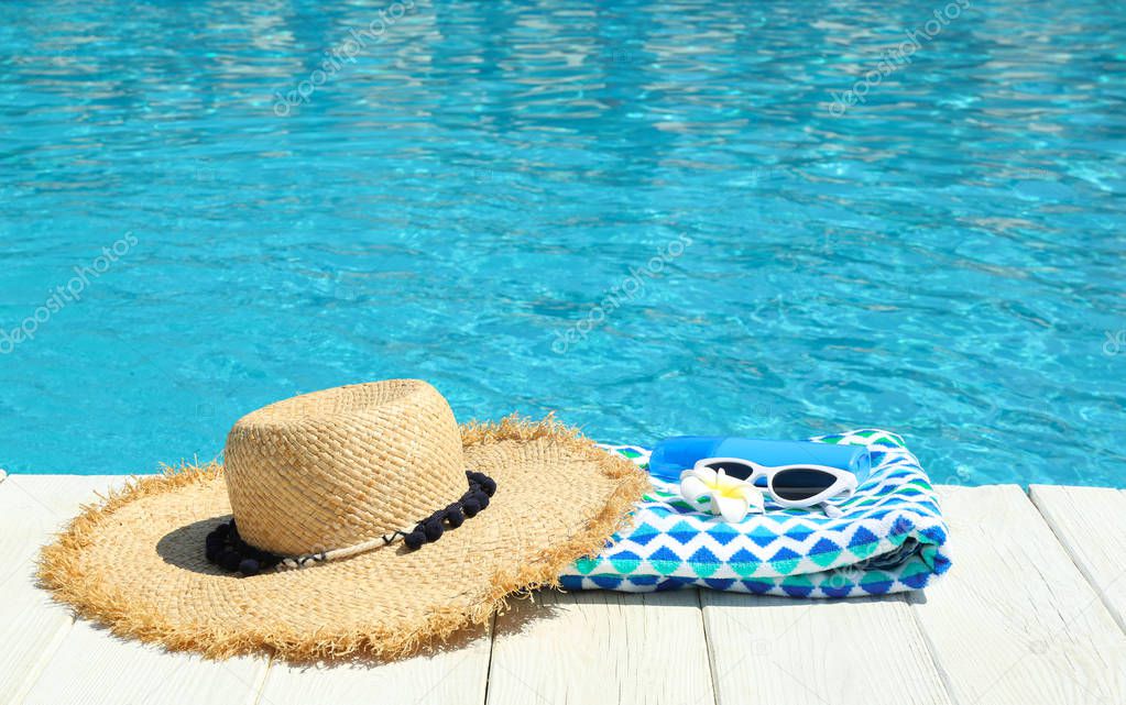 Beach accessories on wooden deck near swimming pool. Space for text