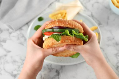 Masanın üstünde lezzetli bir burger tutan bir kadın.