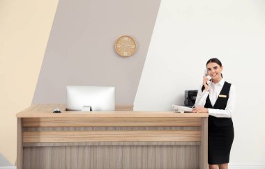 Resepsiyonist modern otelde masa yakınında telefonla konuşuyor