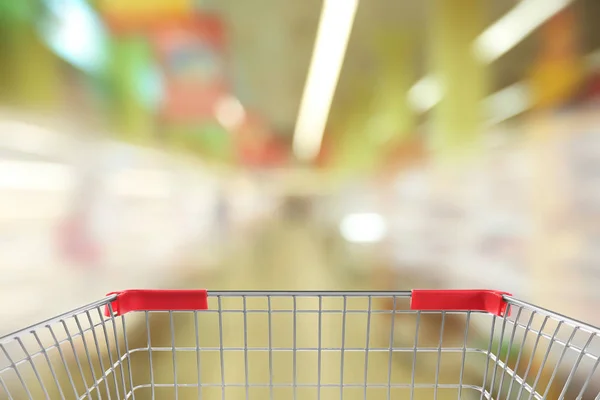 Розмитий вид на супермаркет і порожній кошик для покупок, крупним планом — стокове фото