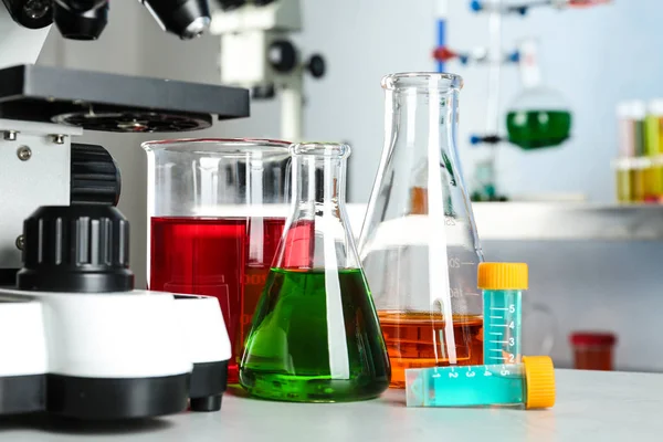 Különböző üvegedények mintákkal és mikroszkóppal a kémiai laboratóriumi asztalon — Stock Fotó