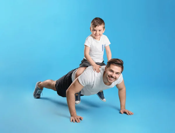 Táta dělá tlačení se synem na zádech proti barevnému pozadí — Stock fotografie