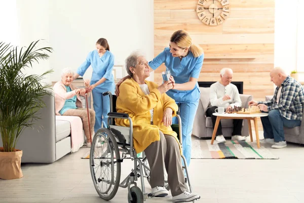 Krankenschwester schenkt älteren Frauen im Rollstuhl im Altenheim ein Glas Wasser. Hilfe für Senioren — Stockfoto