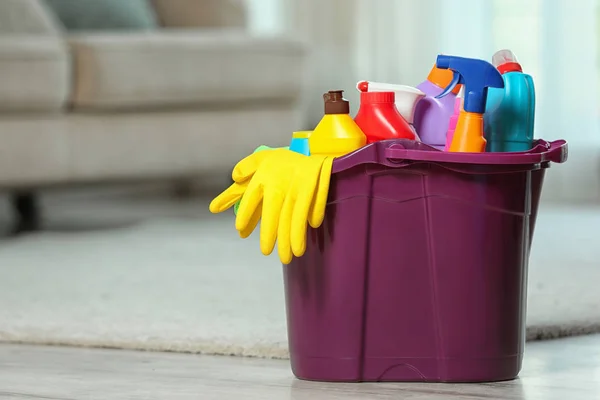 Plastic bucket with different cleaning products on floor indoors, space for text — Stock Photo, Image