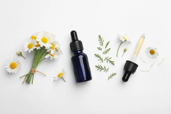 Komposition mit Kamillenblüten und Kosmetikflasche mit ätherischem Öl auf weißem Hintergrund, Draufsicht — Stockfoto