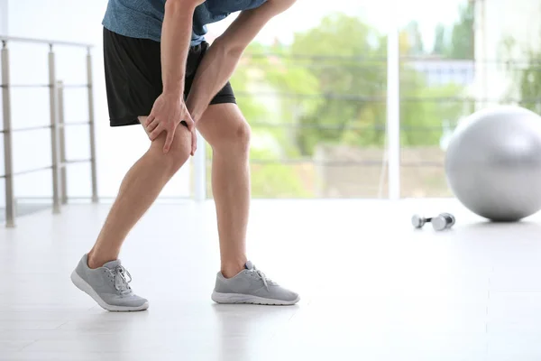 Uomo in abbigliamento sportivo che soffre di dolore al ginocchio in palestra, primo piano — Foto Stock