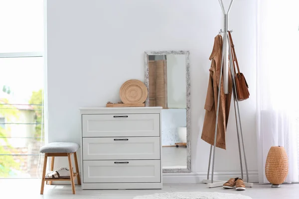 Modern hallway interior with chest of drawers and clothes on hanger stand. Space for text