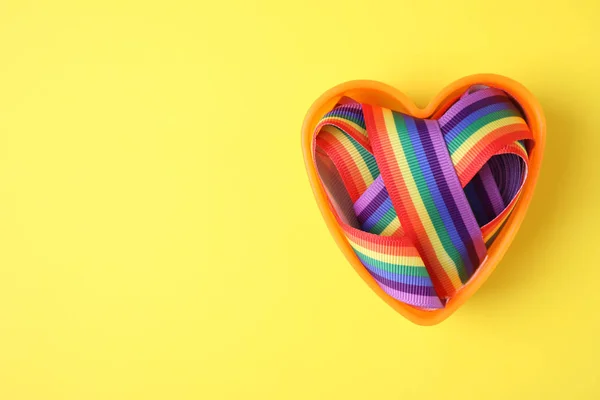 Tvar srdce a zářivá Duhová stuha na barevném pozadí, pohled shora s prostorem pro text. Symbol gayské komunity — Stock fotografie