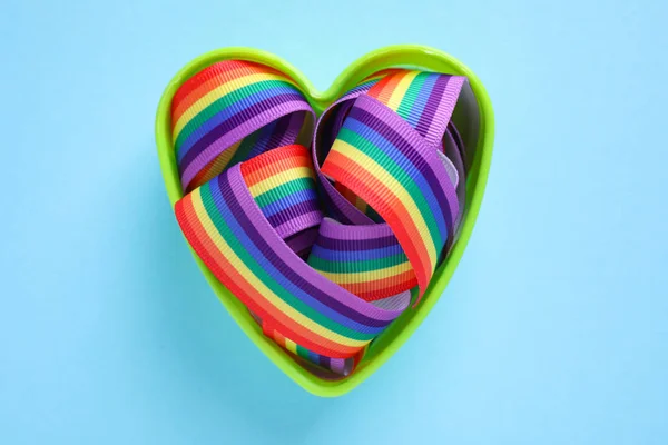 Srdce tvarované jako plíseň s jasnou duhovou stuhou na barevném pozadí, pohled shora. Symbol gayské komunity — Stock fotografie