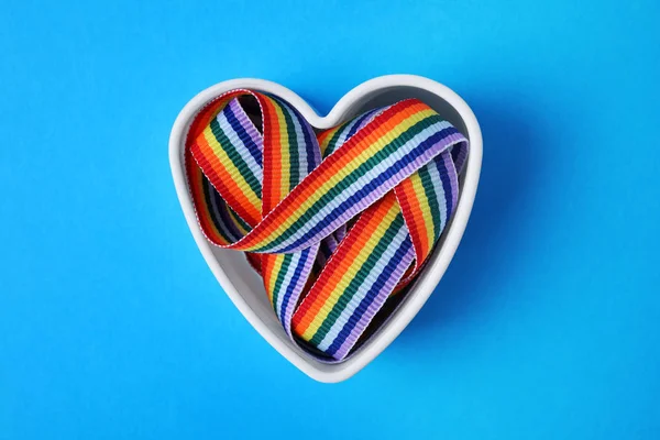 Heart shaped mold with bright rainbow ribbon on color background, top view. Symbol of gay community — Stock Photo, Image