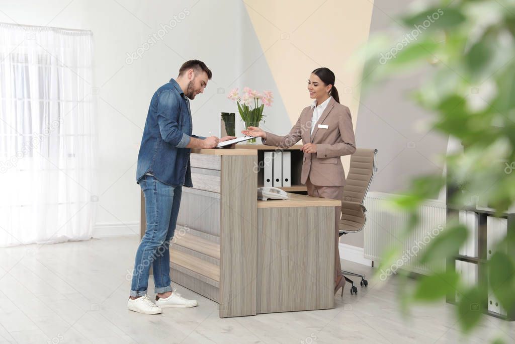 Professional receptionist working with client at desk in modern hotel