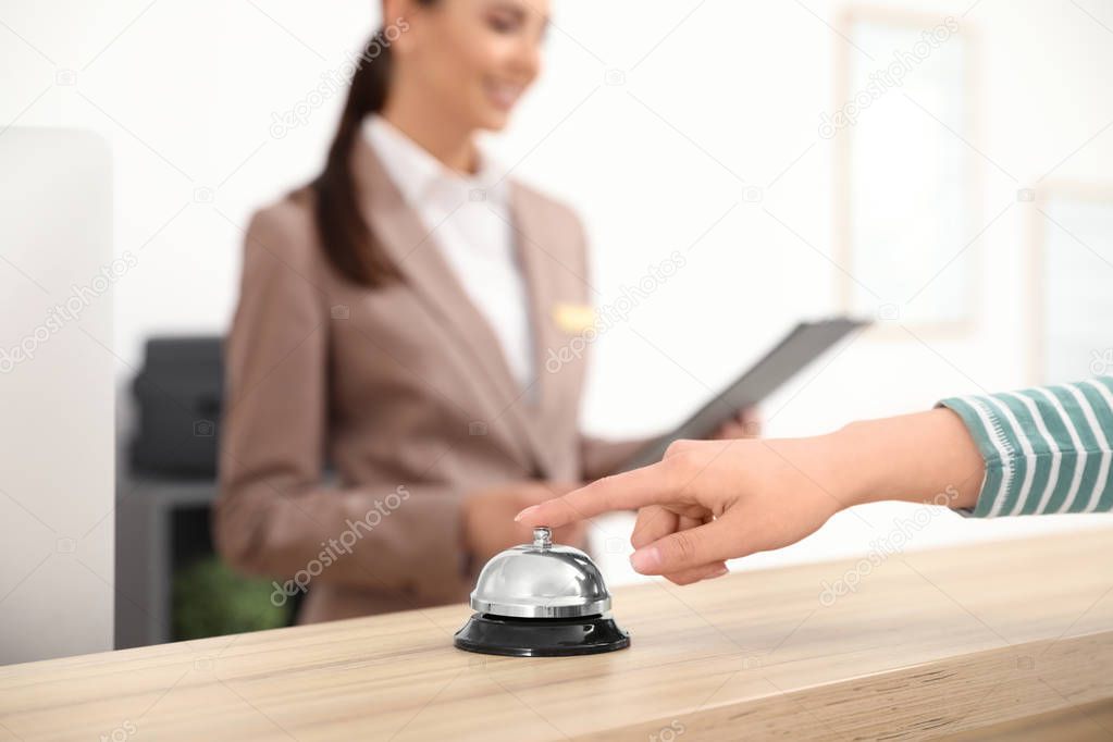 Guest pressing service bell at desk near receptionist in hotel, closeup. Space for text