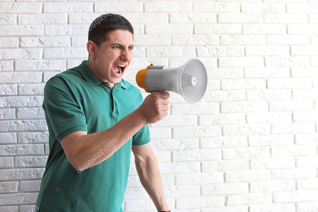 Portrait of young man using megaphone near brick wall. Space for text