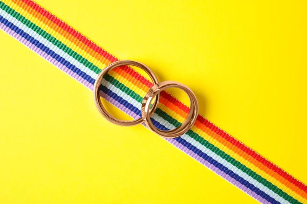 Vigselringar och Rainbow Ribbon på färg bakgrund, uppifrån. Gay-symbol — Stockfoto