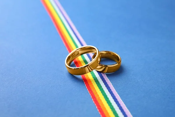 Trouwringen en regenboog lint op kleur achtergrond. Gay symbool — Stockfoto
