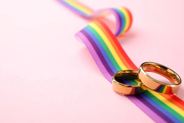 Anillos de boda y cinta de arco iris sobre fondo de color, espacio para el texto. Símbolo gay — Foto de Stock
