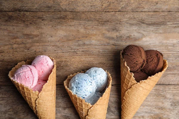 Composição plana com deliciosos sorvetes em cones de waffle na mesa de madeira, espaço para texto — Fotografia de Stock