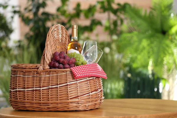 Piknik kosár borral, poharakkal és szőlőkkel, fából készült asztalon homályos háttér, szöveg szóközzel szemben — Stock Fotó