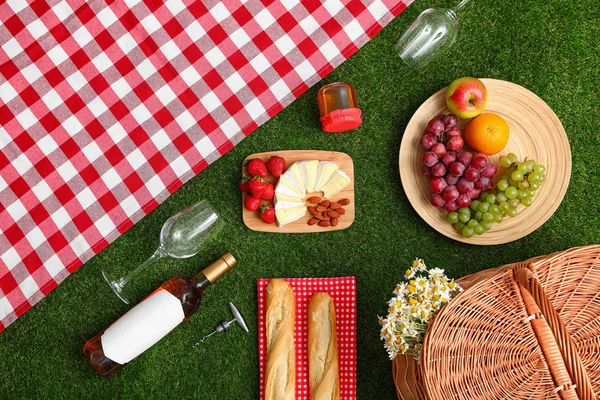 Flache Liegekomposition mit Picknickdecke, Produkten und Wein auf Gras — Stockfoto