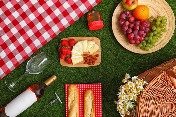 Flache Liegekomposition mit Picknickdecke, Produkten und Wein auf Gras — Stockfoto