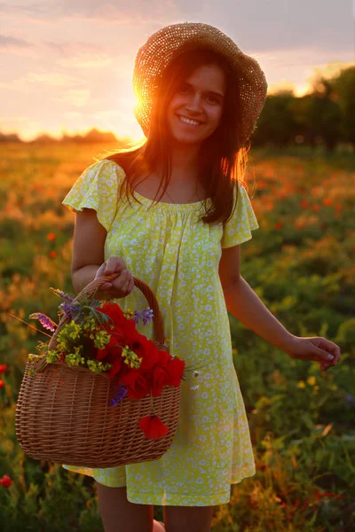 Vrouw met mand van papavers en wilde bloemen in prachtig veld bij zonsondergang — Stockfoto