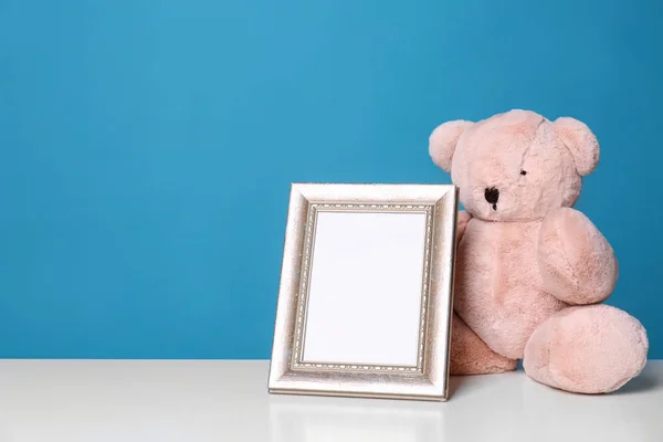 Photo frame and adorable teddy bear on table against color background, space for text. Child room elements — Stock Photo, Image